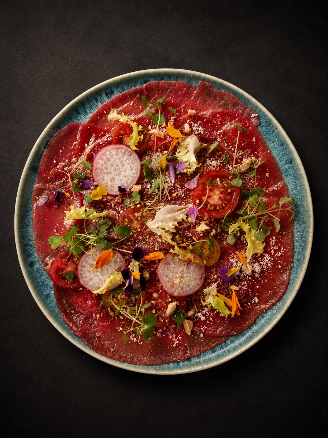 Carpaccio arranged with tomatoes, greens and edible flowers